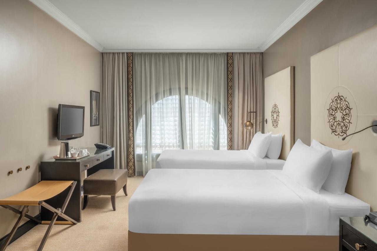 فندق شهد المدينة بإدارة اكور المدينة المنورة المظهر الخارجي الصورة The photo shows a hotel room with a modern and minimalist design. There are two neatly made twin beds with white linens. A small table and an armchair are positioned near the window, which is draped with sheer curtains allowing natural light to enter
