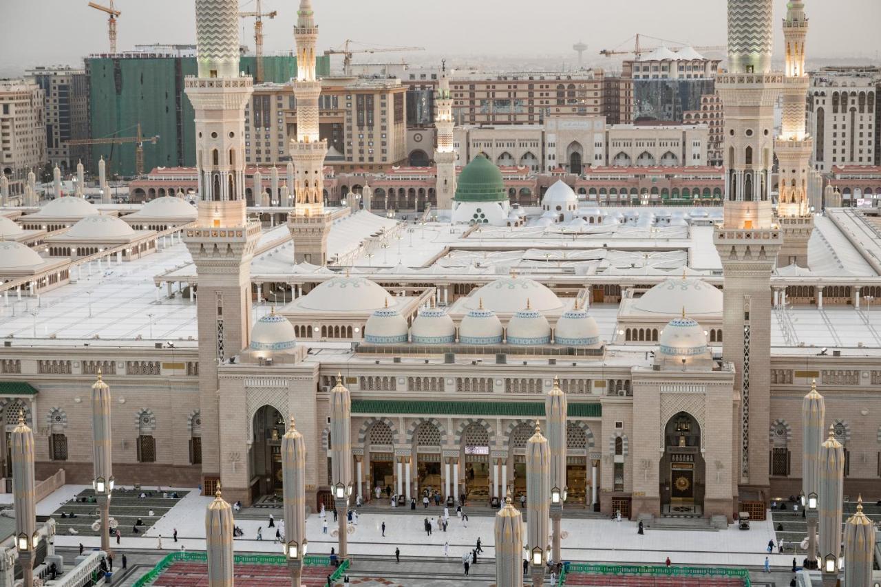 فندق شهد المدينة بإدارة اكور المدينة المنورة المظهر الخارجي الصورة The photo shows an aerial view of a mosque complex, with prominent architectural features such as tall minarets and a large dome. The structure is notable for its intricate design and is likely surrounded by an open courtyard where people are gathere