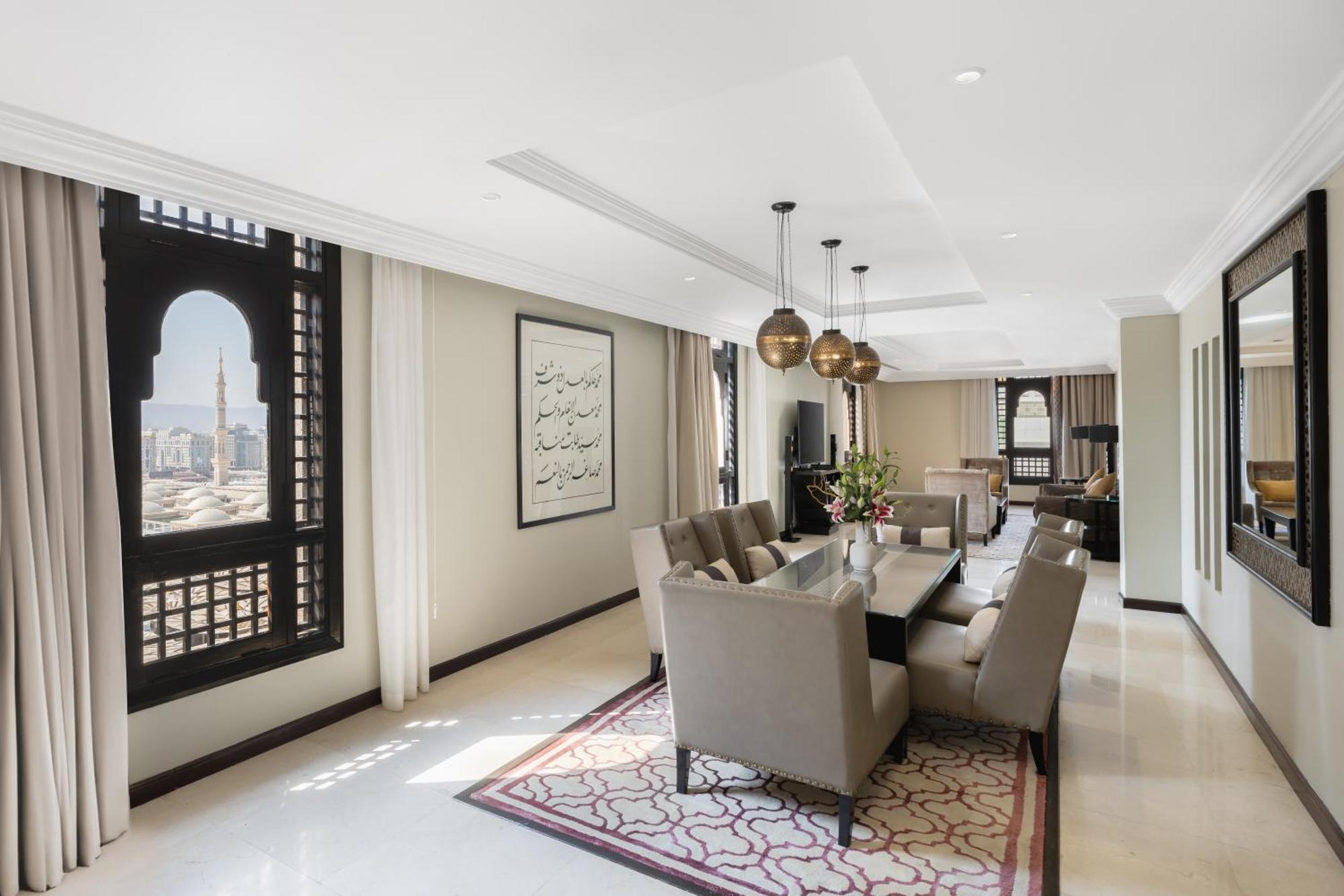 فندق شهد المدينة بإدارة اكور المدينة المنورة المظهر الخارجي الصورة The photo shows a spacious and elegantly designed interior of a living or dining area. The room features a long table surrounded by several plush chairs, suggesting a space for dining or gatherings. 

Large, ornate windows allow natural light to floo
